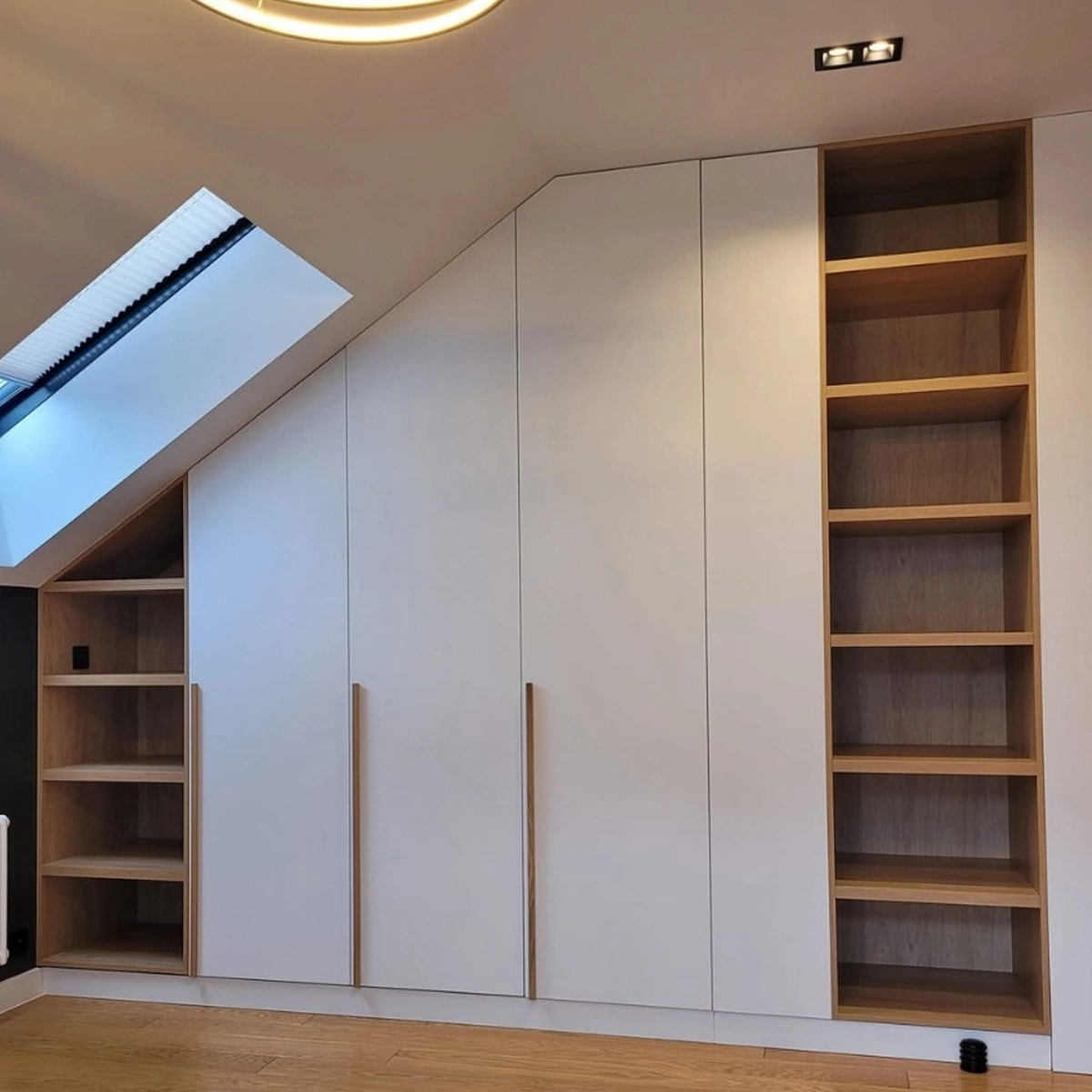 Einbauschrank nach Maß unter einer Dachschräge: weiße grifflose Fronten mit schmalen Holzgriffleisten, kombiniert mit offenen Regalfächern in Eiche, angepasst an Schräge und Kniestock.