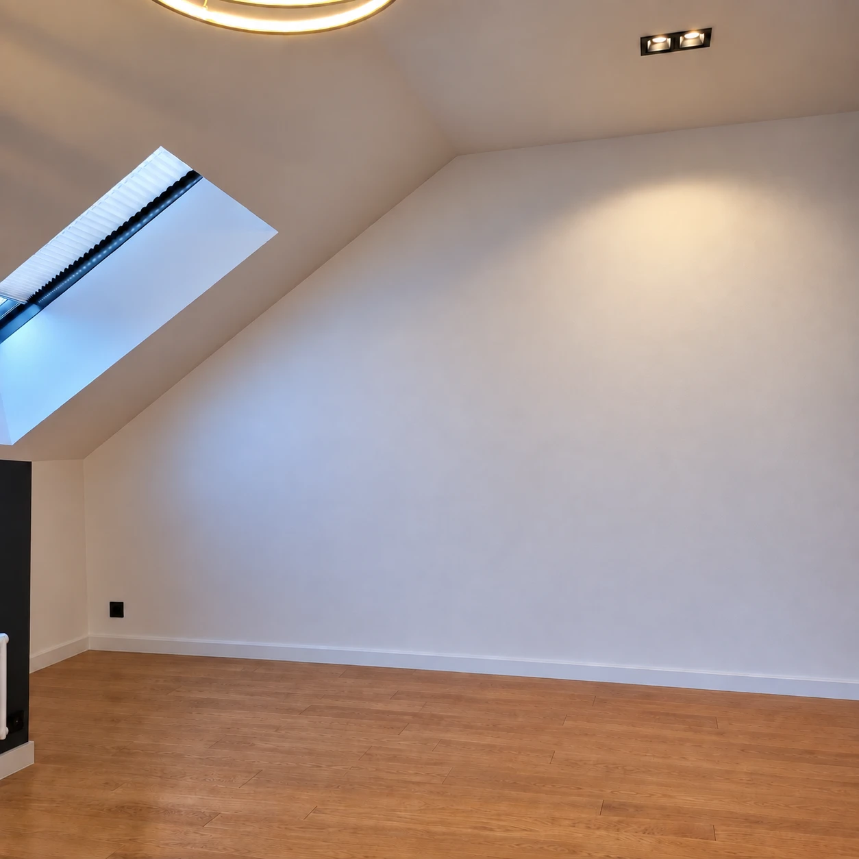 Leeres Dachgeschosszimmer vor dem Einbau: weiße Schräge mit Dachfenster, Holzboden, an der rechten Wand keinerlei Möbel — die gesamte Fläche unter der Schräge liegt ungenutzt.