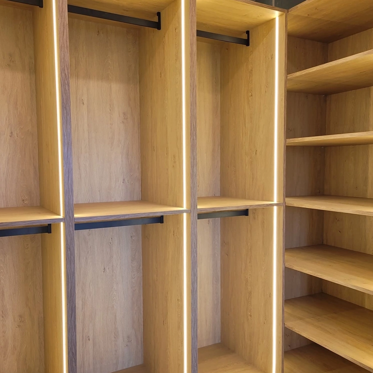 Offenes Ankleidezimmer nach Maß in Holzoptik mit LED-Beleuchtung, Kleiderstangen und offenen Regalfächern, gefertigt von MAGUBO.